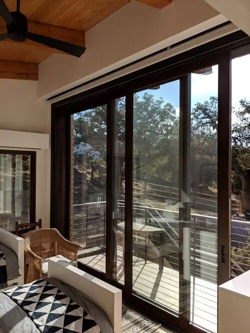 A dark wood clad multi-slide door opening from a bedroom onto a hillside deck